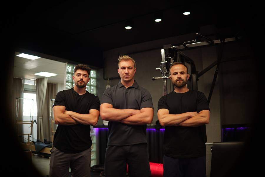 ACK Fitness'ta kollarını kavuşturmuş üç erkek antrenör